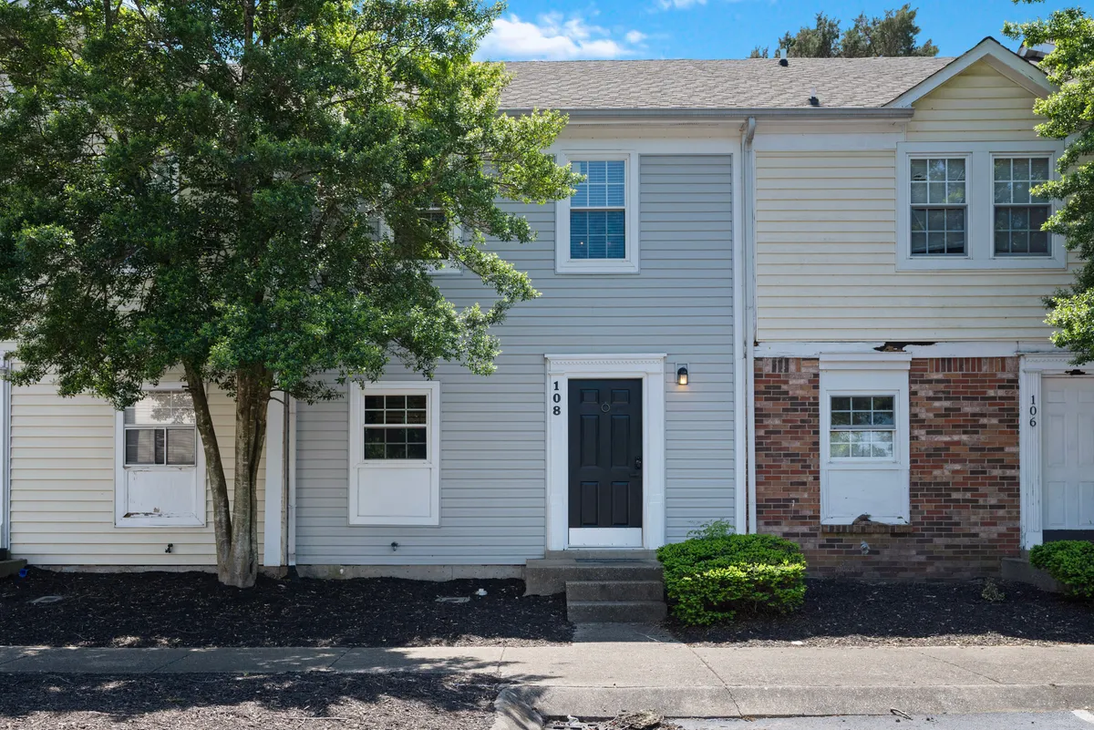 A welcoming exterior view of the property, showcasing the front door surrounded by trees, well-kept landscaping, and large windows. The scene suggests opportunities for outdoor relaxation and social gatherings, with the inviting entry hinting at a friendly, group-oriented environment.