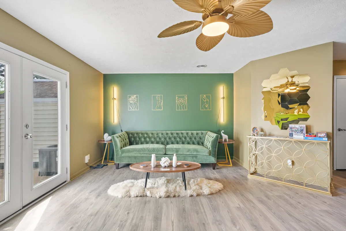 A stylish and comfortable living space featuring a green velvet sofa, round coffee table, golden accents, and wall art. The room is arranged for social gatherings, relaxing after work, or team meetings.