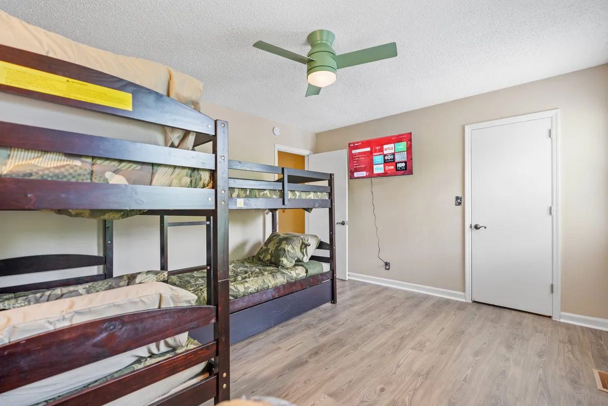 A cozy interior shot of a bedroom with multiple bunk beds, a TV mounted on the wall, and a ceiling fan overhead. The arrangement creates a playful and comfortable space, ideal for kids or groups to unwind, watch TV, and enjoy each other's company.